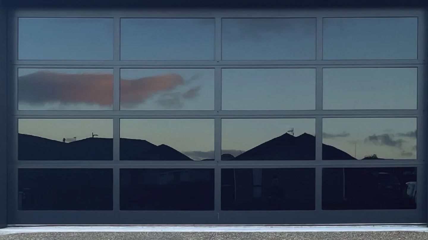Aluminium glass panel garage door with tempered glass sections on a rendered house, design rendering