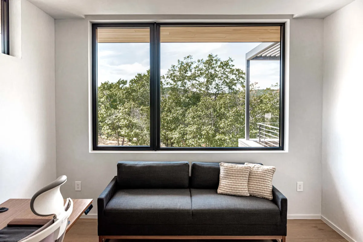 Living room with a wide aluminium window, roller blind and black sofa